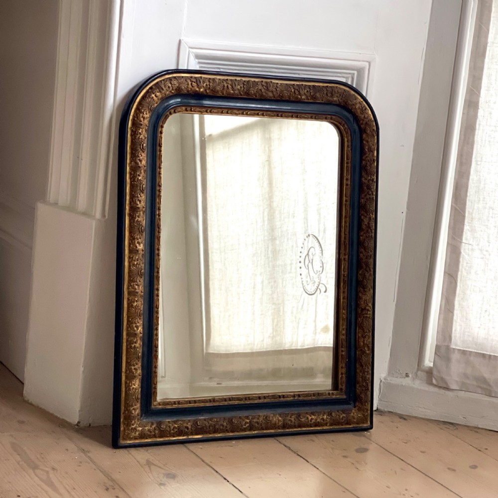 An arched antique French mirror featuring a dark painted outer border and a giltwood frame carved with foliate patterns.
