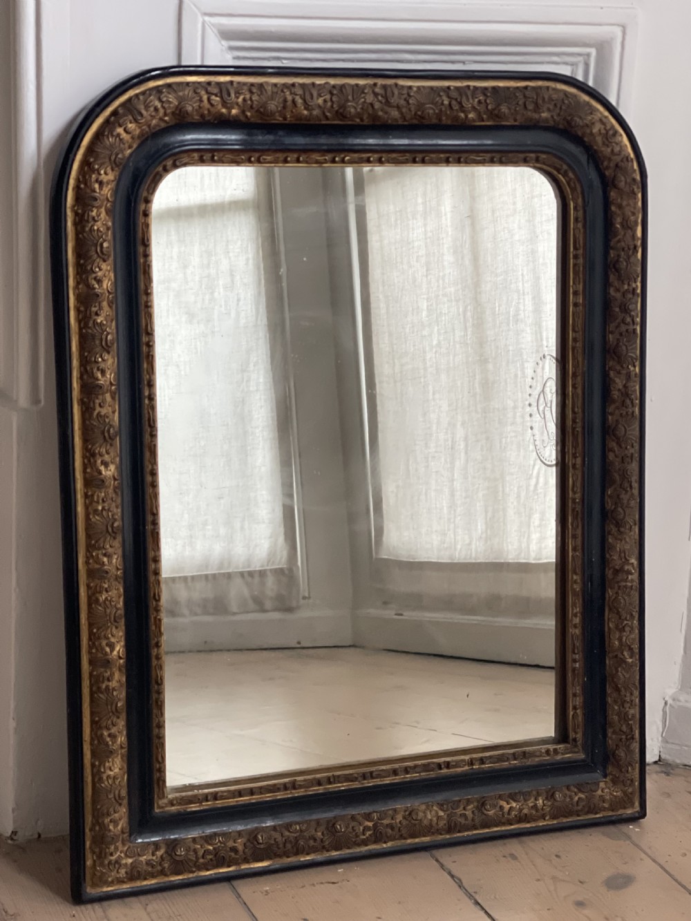 An arched antique French mirror featuring a dark painted outer border and a giltwood frame carved with foliate patterns. View VII