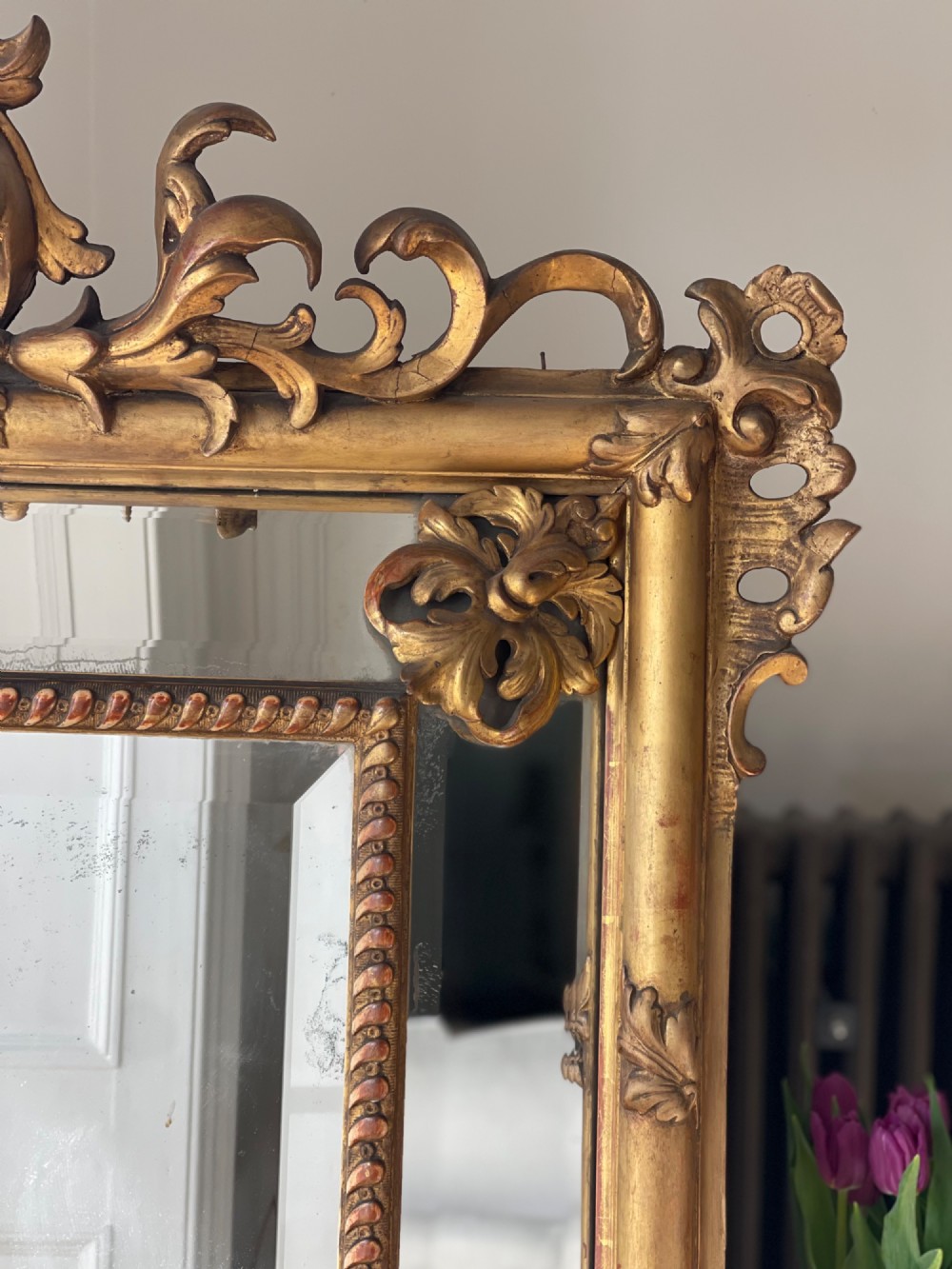 A large antique French giltwood wall mirror featuring carved acanthus cresting, corner flourishes, and bevelled mercury glass. View II
