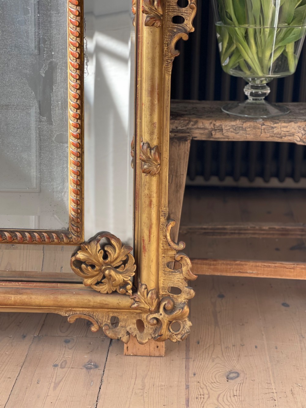 A large antique French giltwood wall mirror featuring carved acanthus cresting, corner flourishes, and bevelled mercury glass. View III