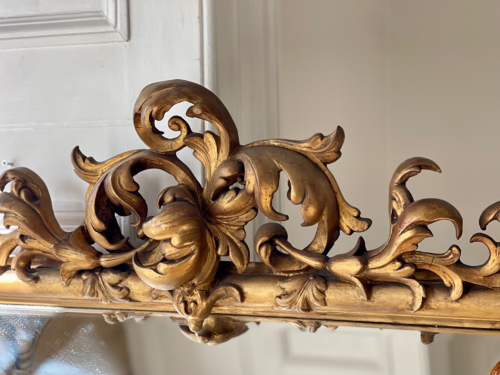 A large antique French giltwood wall mirror featuring carved acanthus cresting, corner flourishes, and bevelled mercury glass. View IV