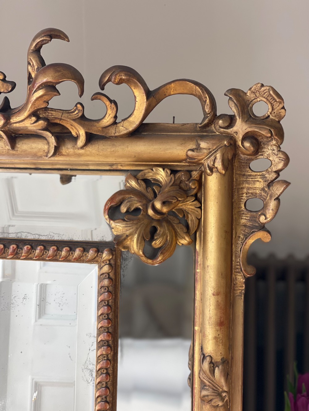 A large antique French giltwood wall mirror featuring carved acanthus cresting, corner flourishes, and bevelled mercury glass. View V