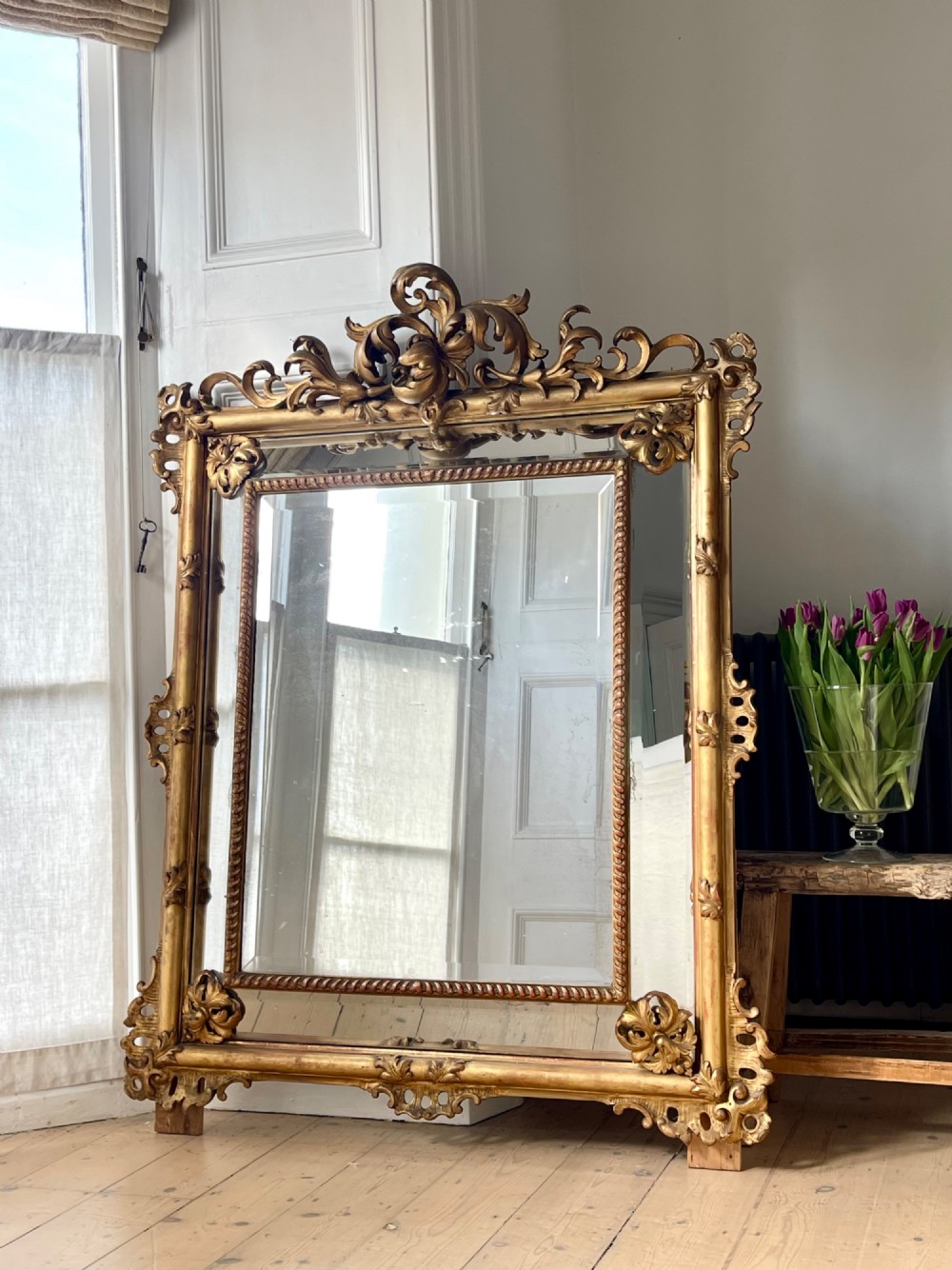A large antique French giltwood wall mirror featuring carved acanthus cresting, corner flourishes, and bevelled mercury glass. View VII