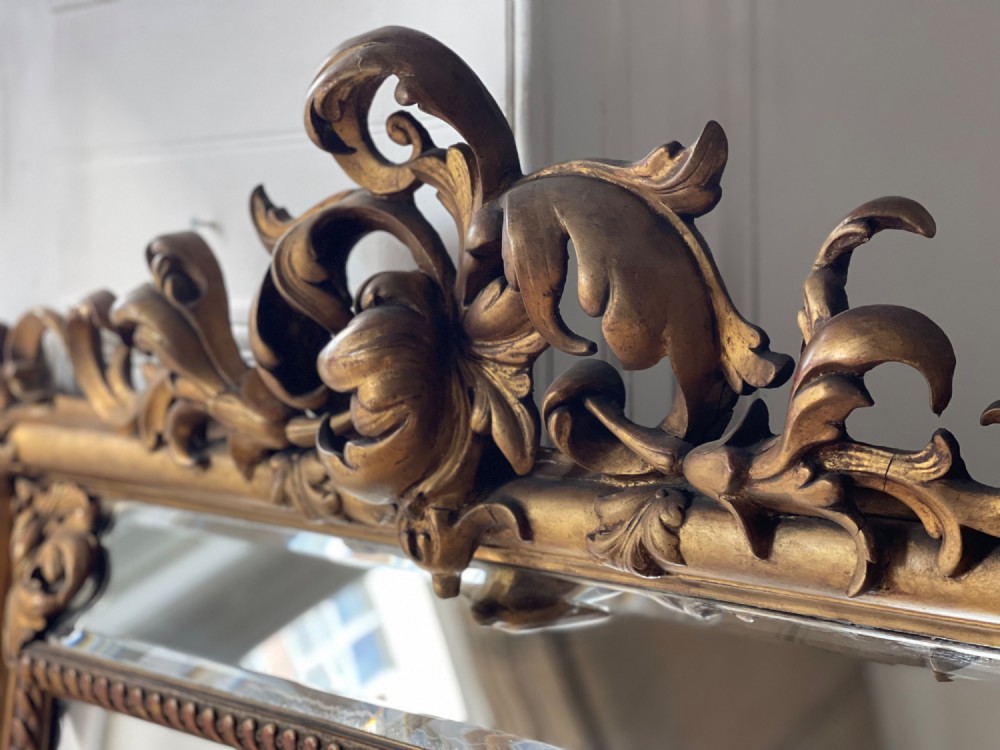 A large antique French giltwood wall mirror featuring carved acanthus cresting, corner flourishes, and bevelled mercury glass. View IX