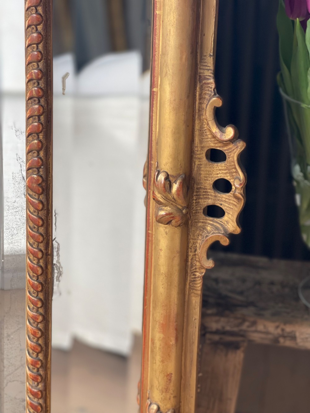 A large antique French giltwood wall mirror featuring carved acanthus cresting, corner flourishes, and bevelled mercury glass. View X