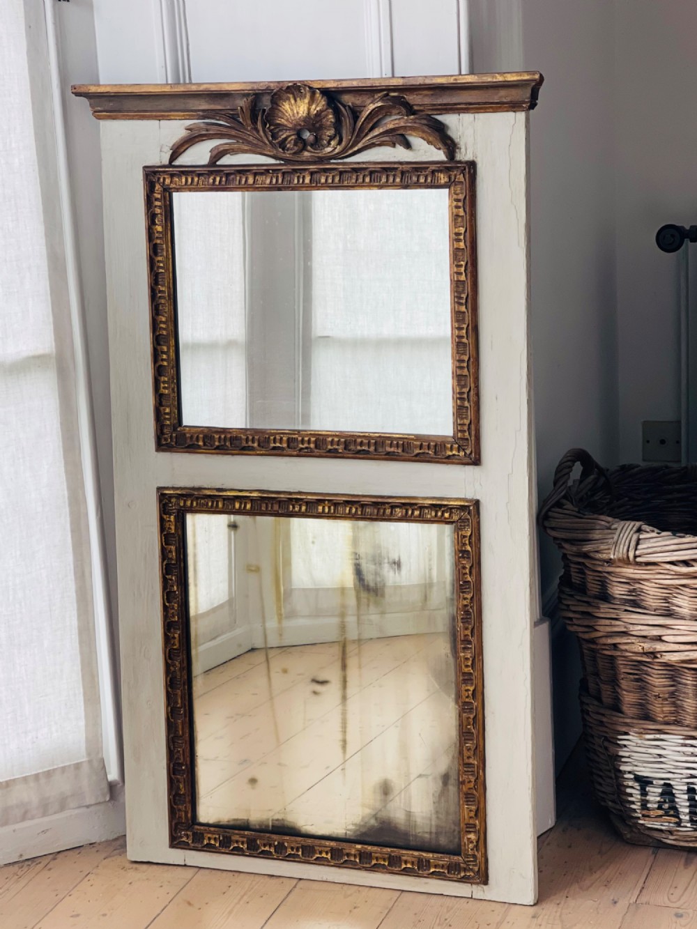 A tall rectangular antique French trumeau mirror featuring two glass panels within a painted cream frame with gilded carved mouldings and a shell crest.