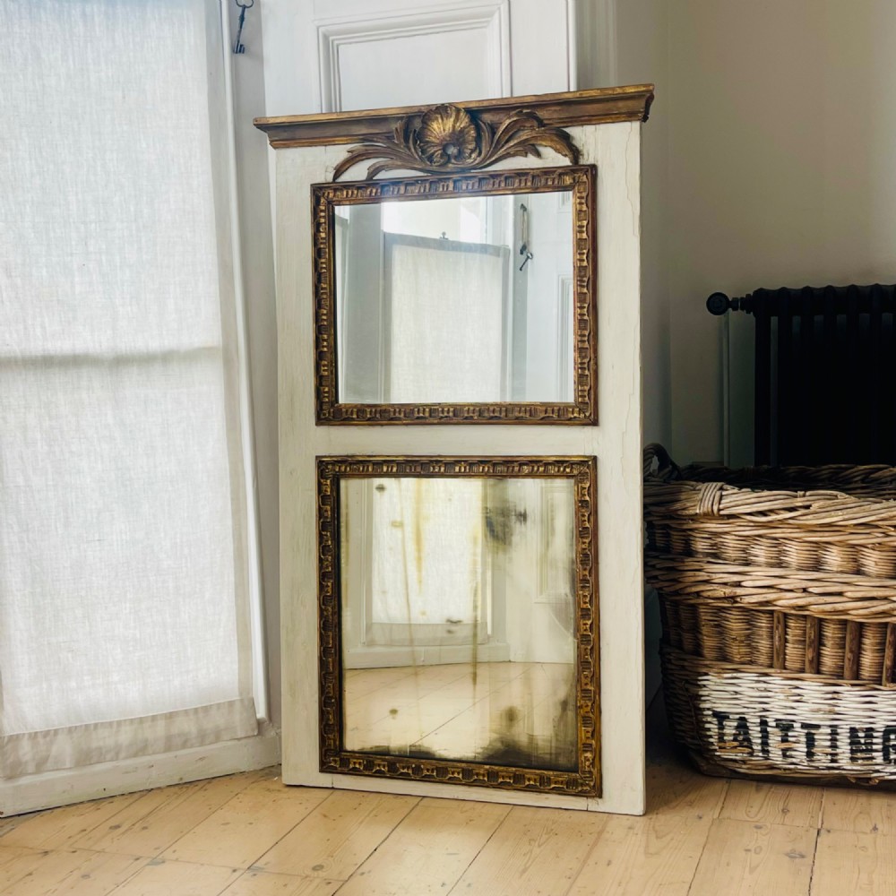 A tall rectangular antique French trumeau mirror featuring two glass panels within a painted cream frame with gilded carved mouldings and a shell crest. View II