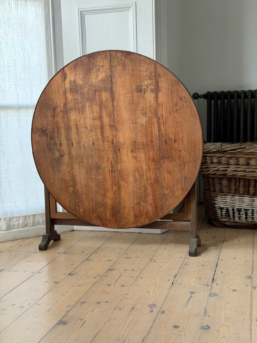 An antique French wooden vendange table featuring a circular plank top shown tilted vertically on a wooden trestle frame base.