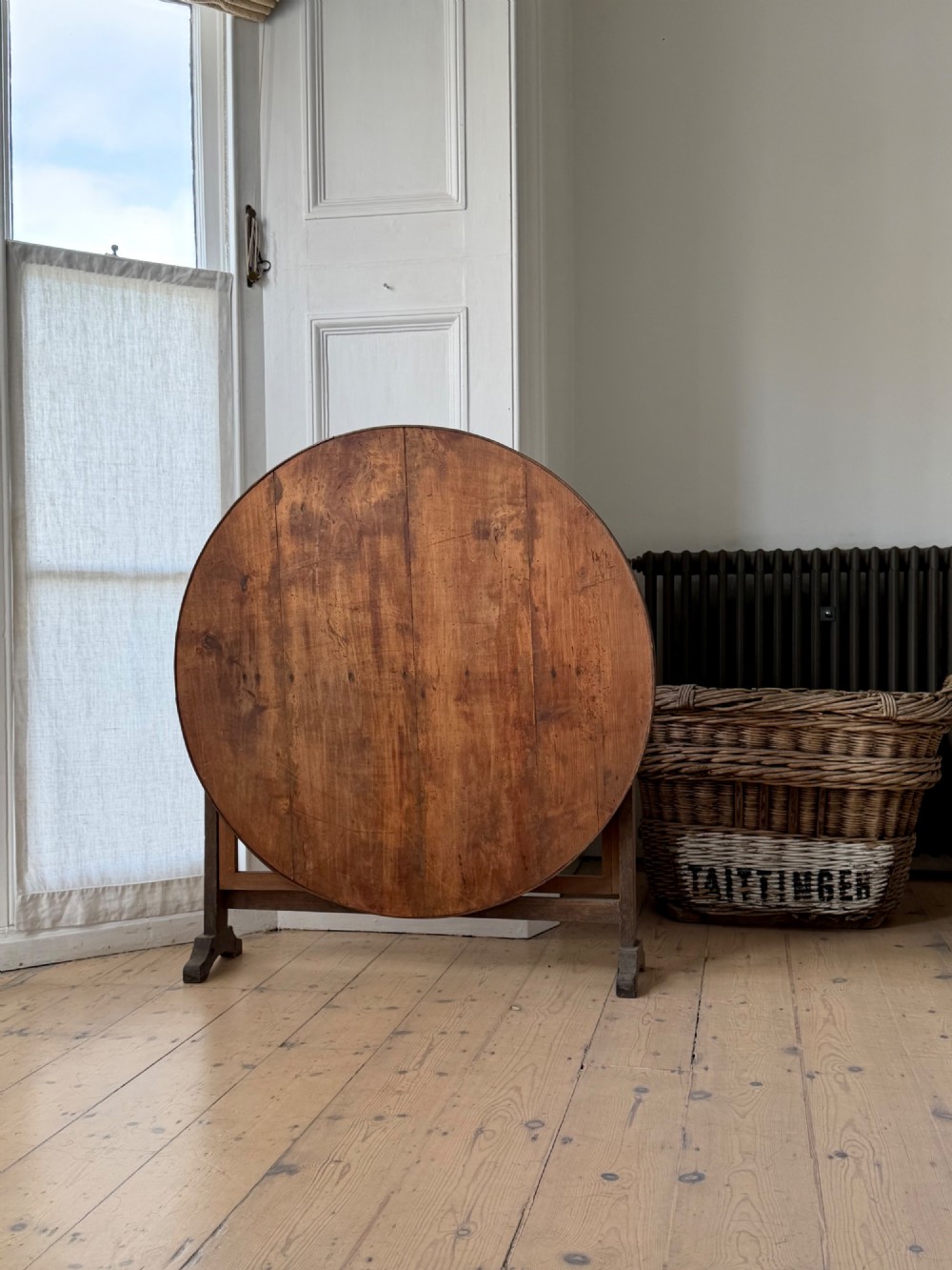 An antique French wooden vendange table featuring a circular plank top shown tilted vertically on a wooden trestle frame base. View IV