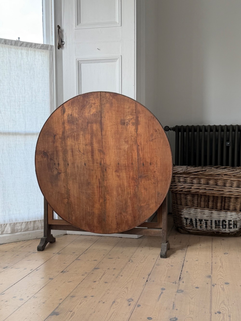 An antique French wooden vendange table featuring a circular plank top shown tilted vertically on a wooden trestle frame base. View V
