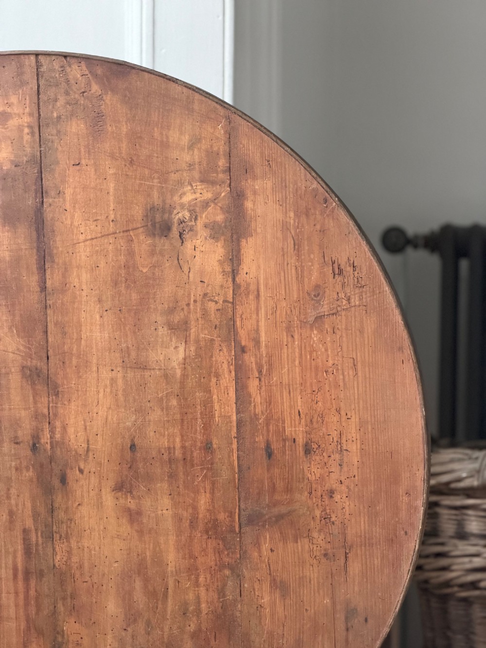An antique French wooden vendange table featuring a circular plank top shown tilted vertically on a wooden trestle frame base. View VI
