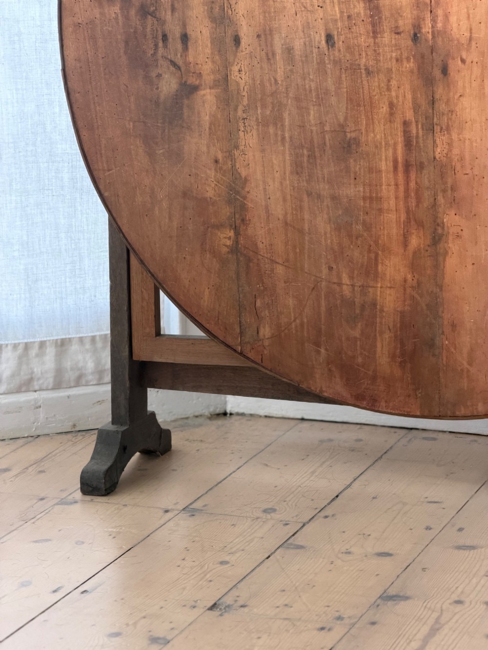 An antique French wooden vendange table featuring a circular plank top shown tilted vertically on a wooden trestle frame base. View VII