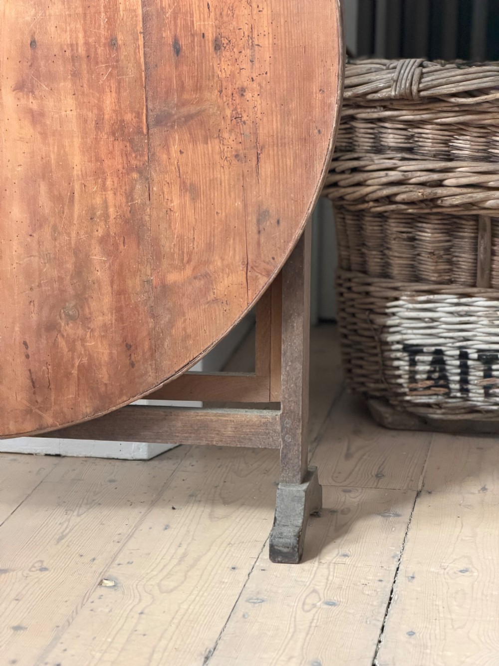 An antique French wooden vendange table featuring a circular plank top shown tilted vertically on a wooden trestle frame base. View VIII