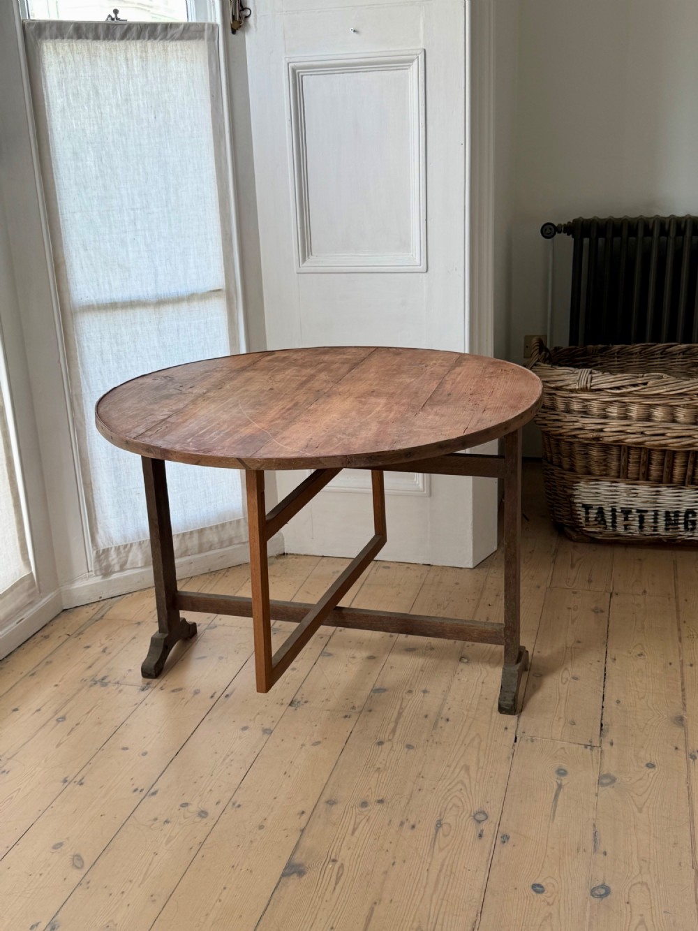 An antique French wooden vendange table featuring a circular plank top shown tilted vertically on a wooden trestle frame base. View IX