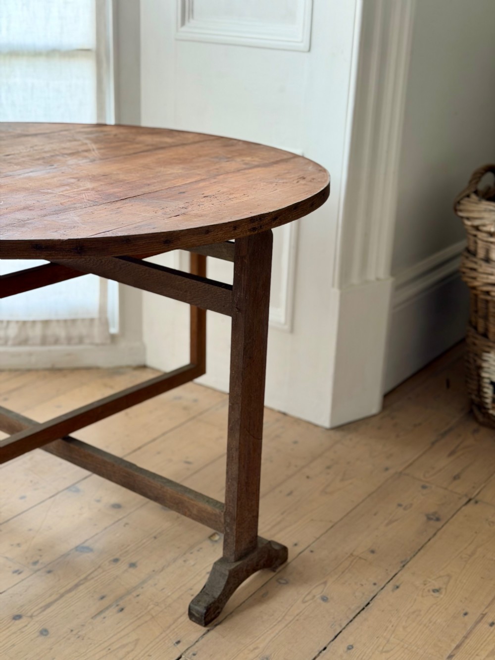 An antique French wooden vendange table featuring a circular plank top shown tilted vertically on a wooden trestle frame base. View XI