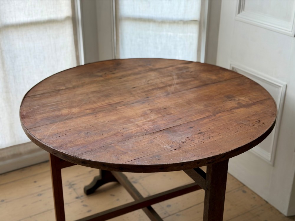 An antique French wooden vendange table featuring a circular plank top shown tilted vertically on a wooden trestle frame base. View XIII