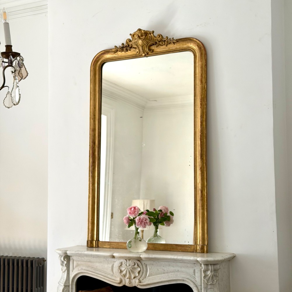 An antique French Louis Philippe wall mirror featuring a gilt frame with rounded upper corners, beaded inner border, and a carved crest.