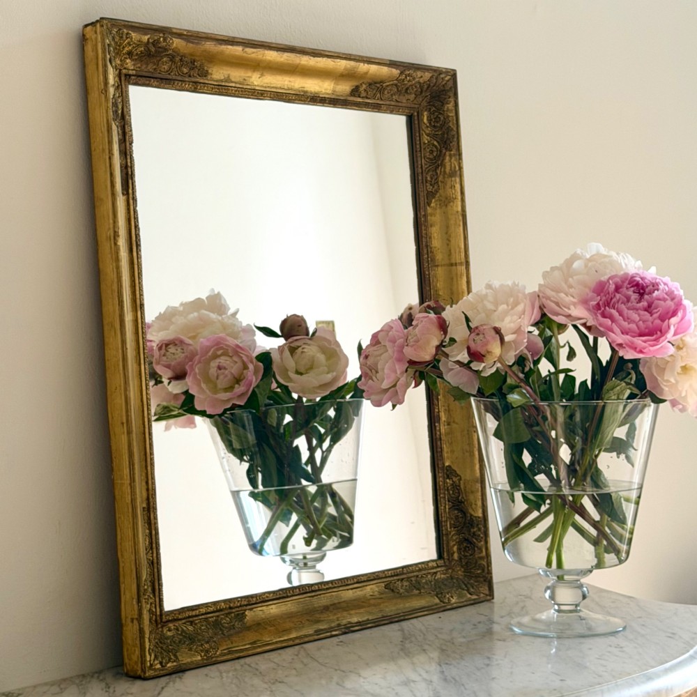A rectangular antique French mirror framed in gold giltwood with ornate carved corner spandrels and subtle beaded borders.