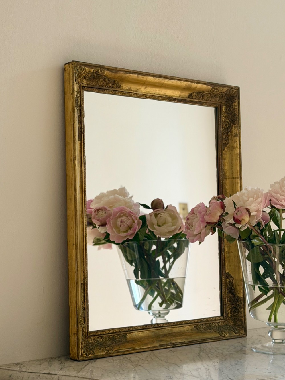 A rectangular antique French mirror framed in gold giltwood with ornate carved corner spandrels and subtle beaded borders. View IV