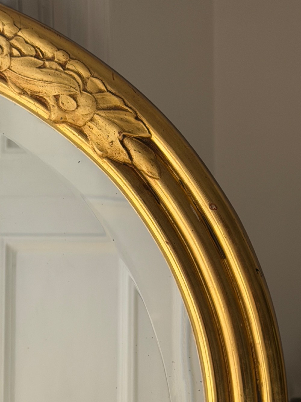 An arched tall mirror featuring a gilded gold frame with fluted side moulding and a carved floral crest. View IX
