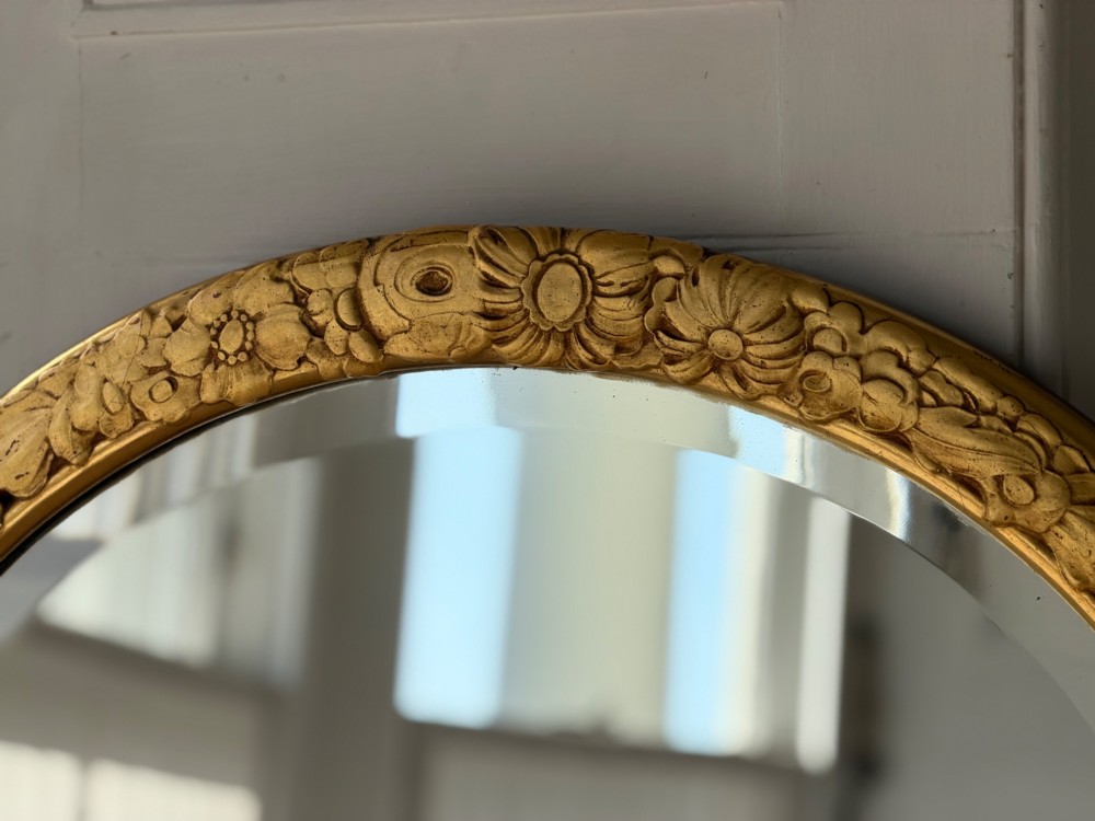 An arched tall mirror featuring a gilded gold frame with fluted side moulding and a carved floral crest. View X