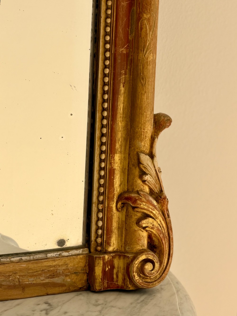 A tall arched antique French wall mirror featuring a gold leaf frame with a carved crest and beaded inner border. View II