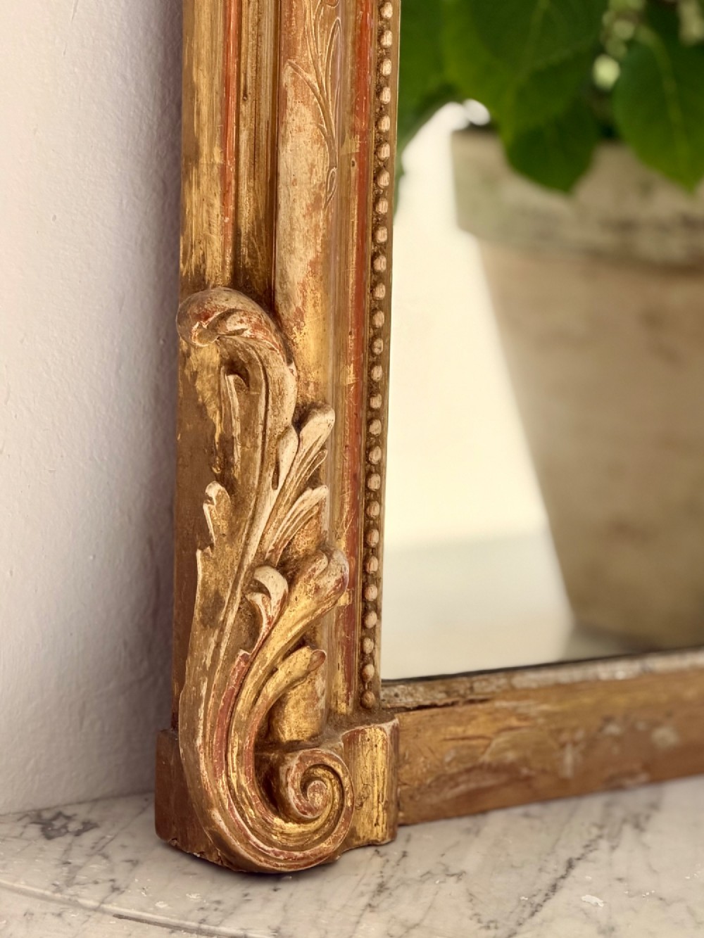 A tall arched antique French wall mirror featuring a gold leaf frame with a carved crest and beaded inner border. View III