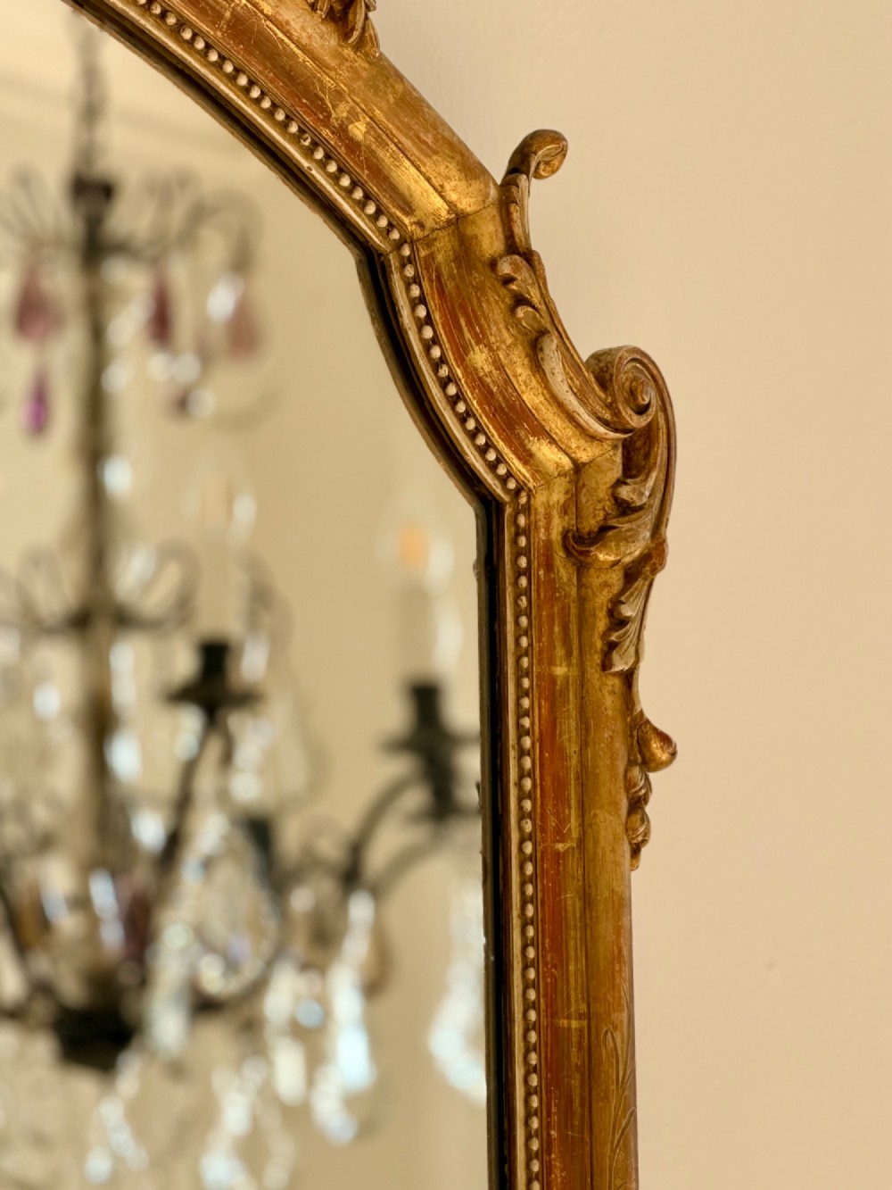 A tall arched antique French wall mirror featuring a gold leaf frame with a carved crest and beaded inner border. View IV