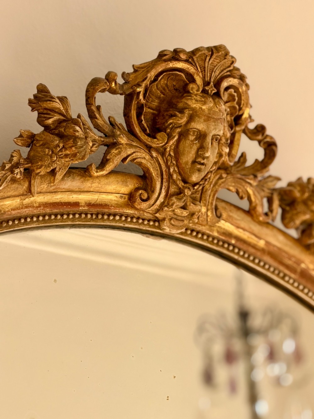 A tall arched antique French wall mirror featuring a gold leaf frame with a carved crest and beaded inner border. View V