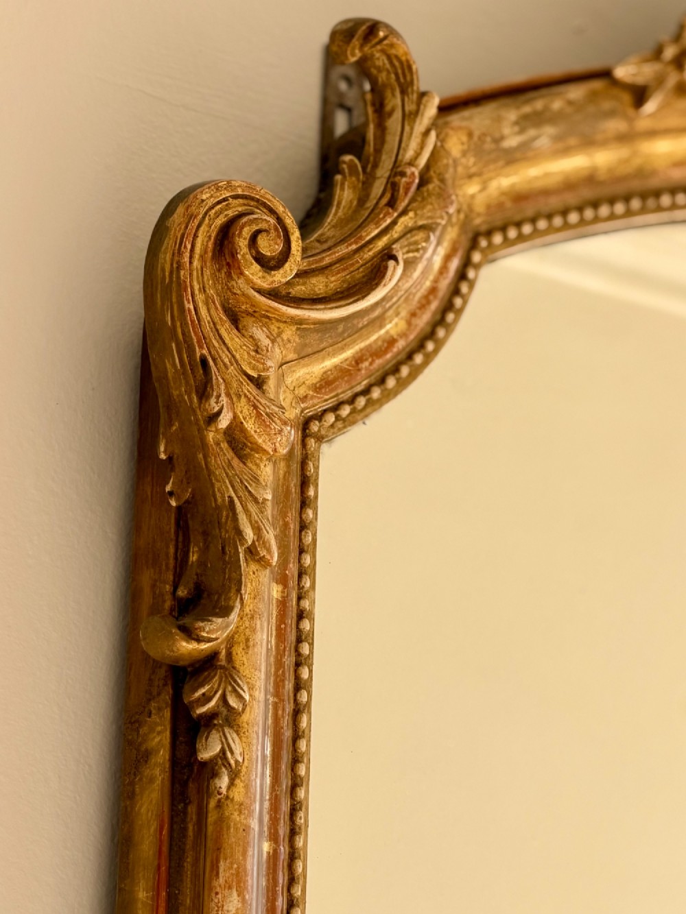 A tall arched antique French wall mirror featuring a gold leaf frame with a carved crest and beaded inner border. View VII