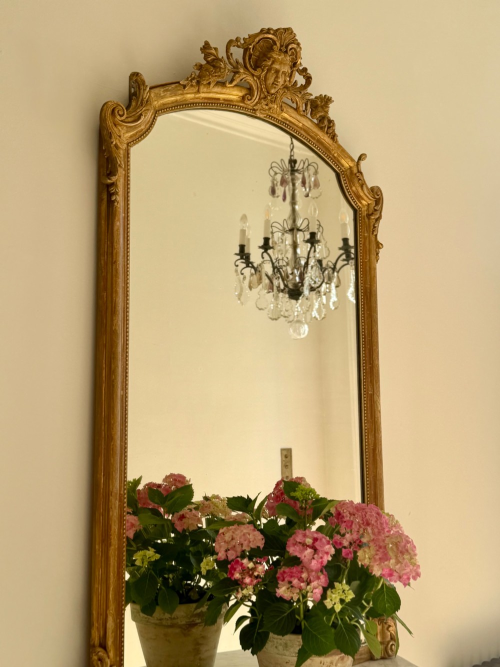 A tall arched antique French wall mirror featuring a gold leaf frame with a carved crest and beaded inner border. View VIII