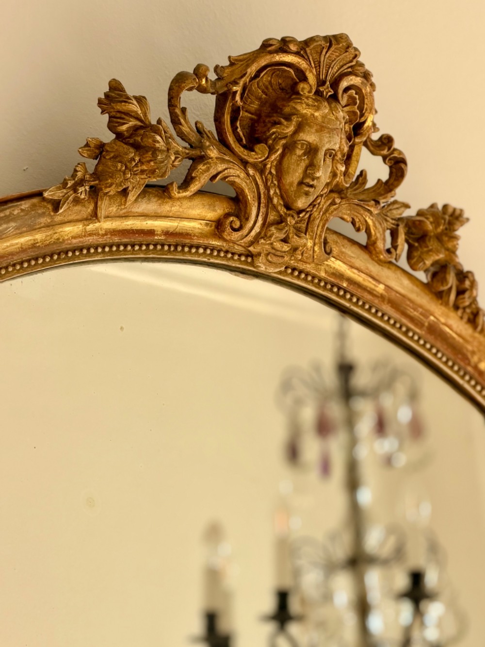 A tall arched antique French wall mirror featuring a gold leaf frame with a carved crest and beaded inner border. View IX