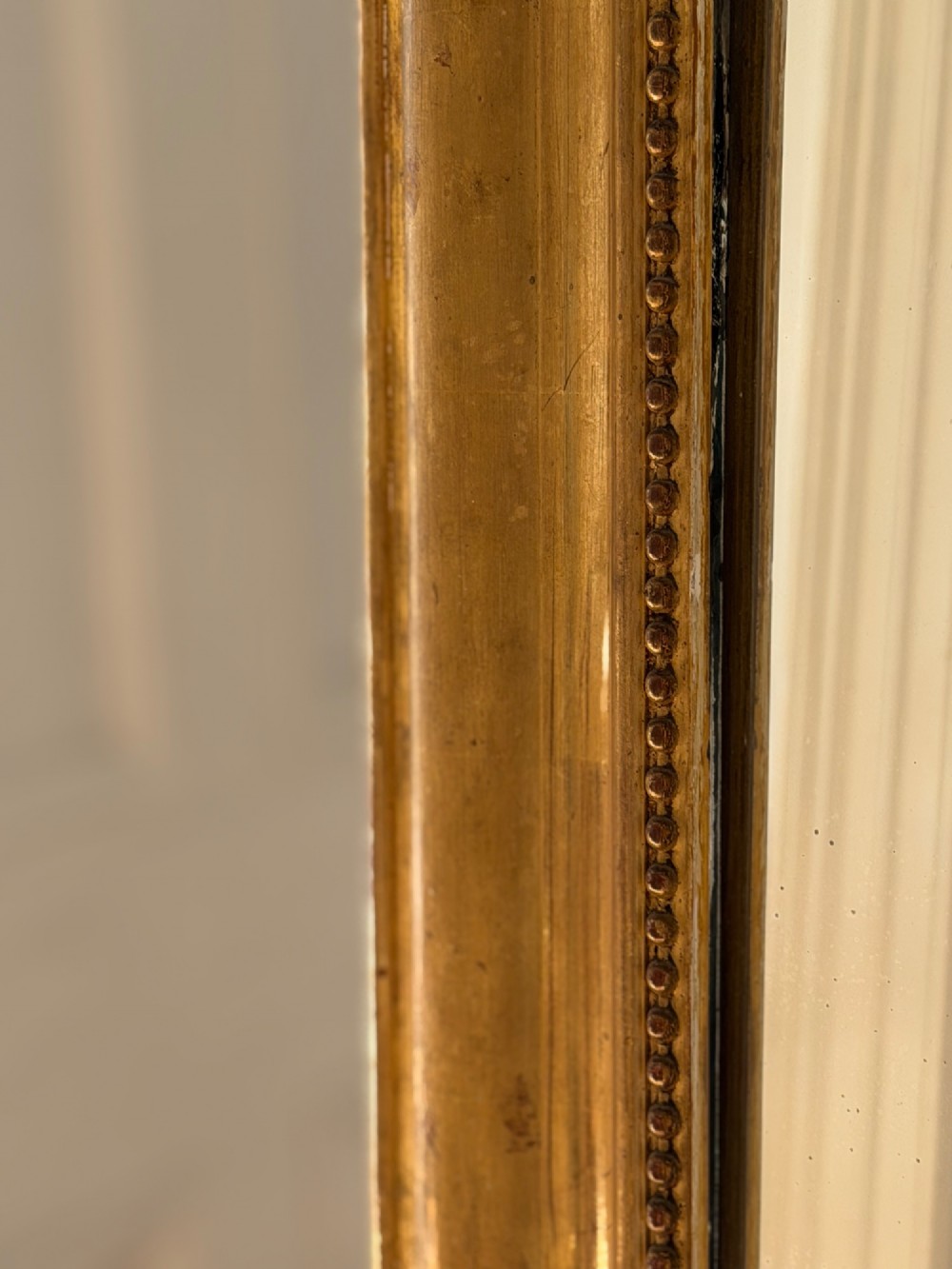 An antique French Louis Philippe wall mirror featuring a gilt frame with rounded upper corners, beaded inner border, and a carved crest. View VII