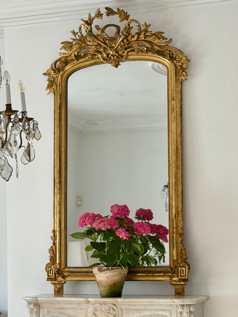 A tall antique French giltwood overmantel mirror featuring an arched frame topped with an ornate carved crest. View V