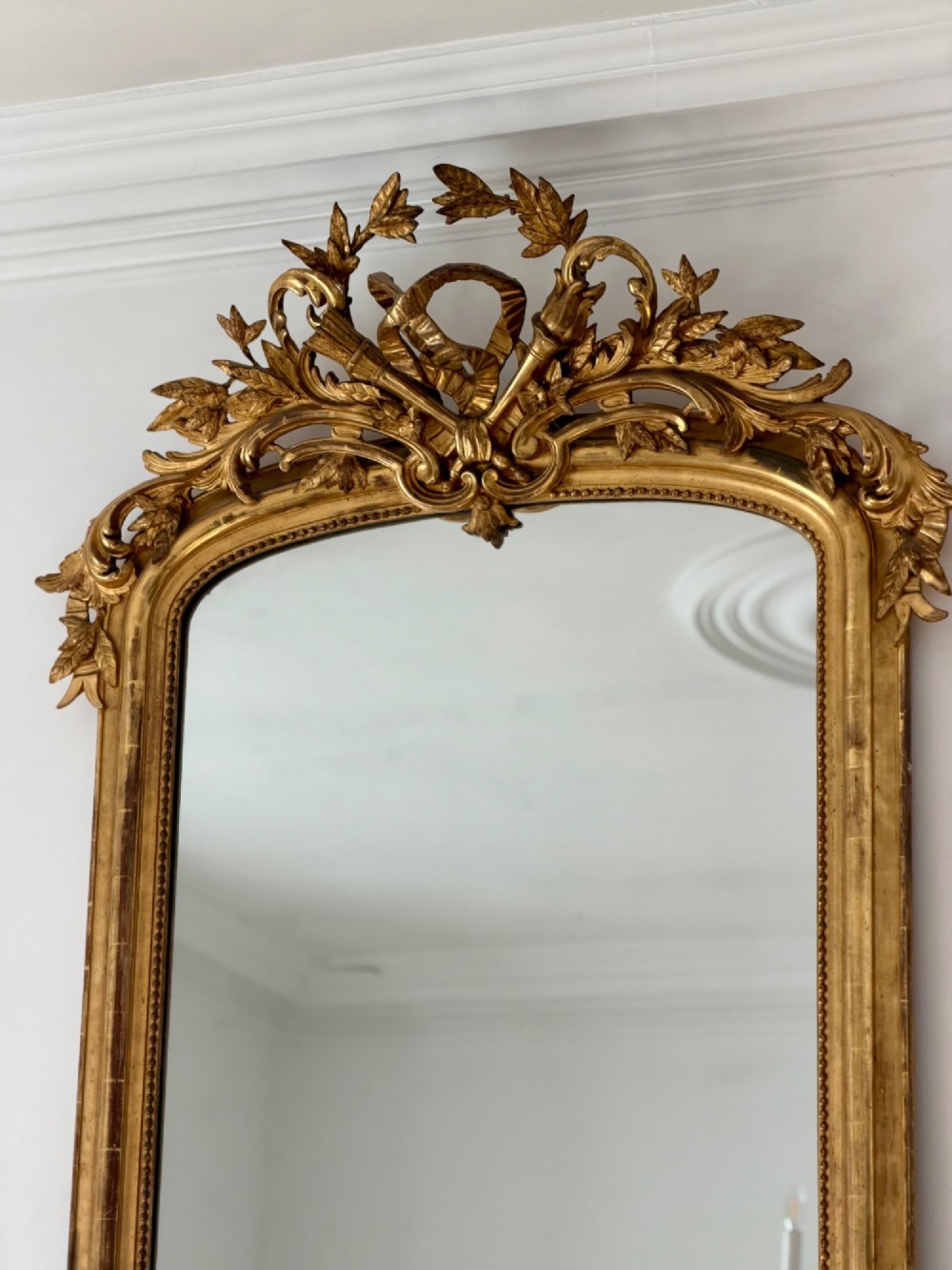 A tall antique French giltwood overmantel mirror featuring an arched frame topped with an ornate carved crest. View VI