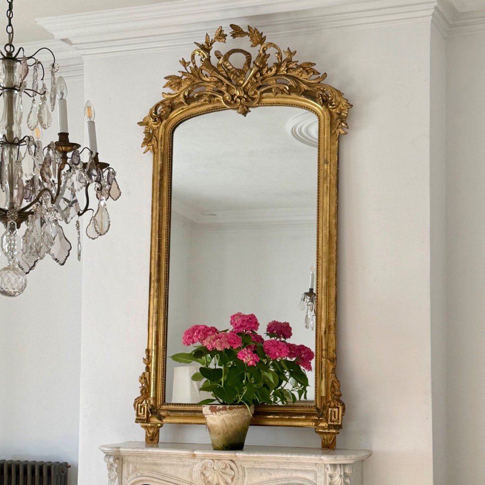A tall antique French giltwood overmantel mirror featuring an arched frame topped with an ornate carved crest.