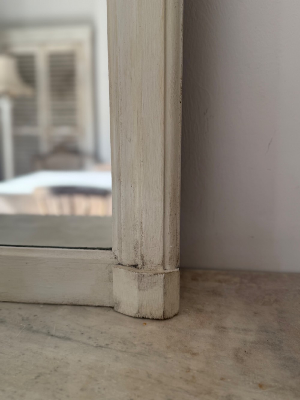 A tall arched mirror featuring a cream painted wooden frame resting on a surface. View IV