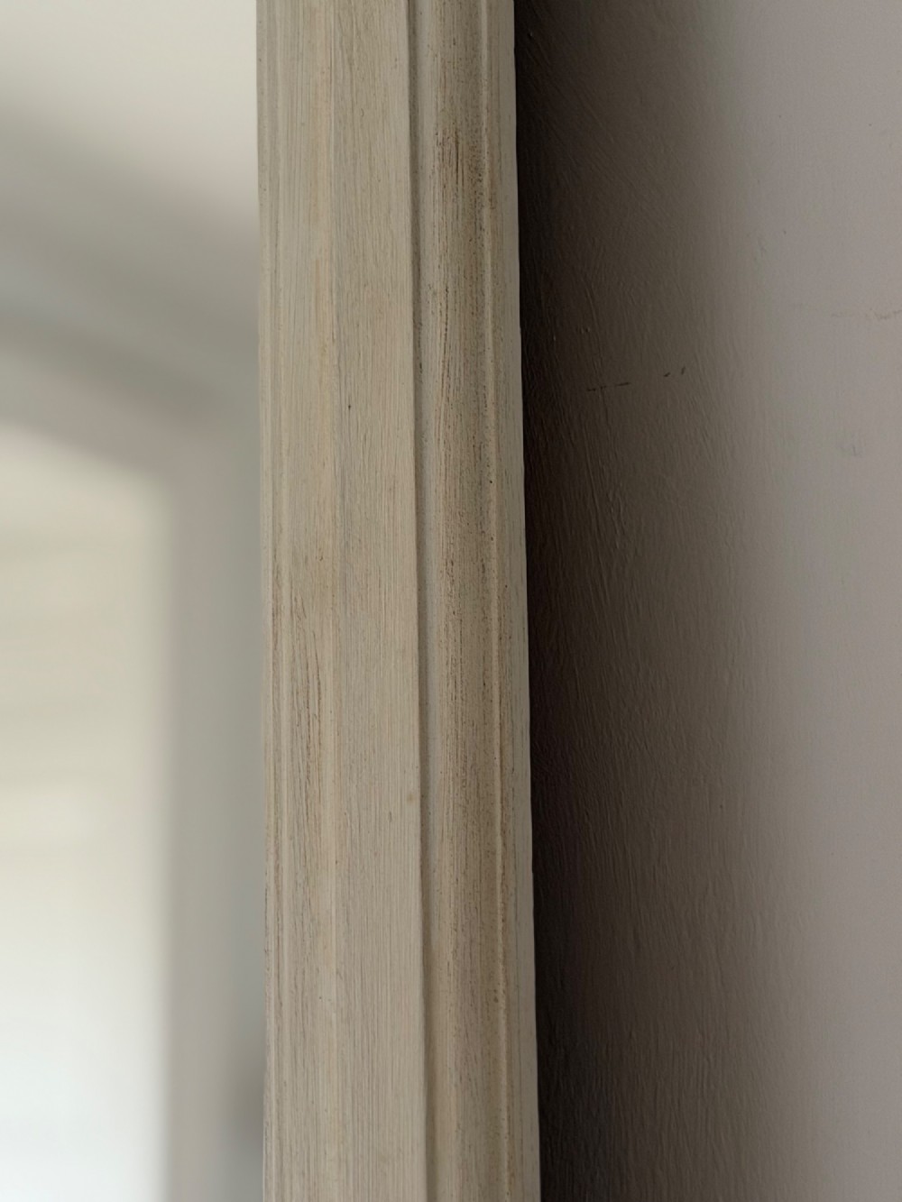 A tall arched mirror featuring a cream painted wooden frame resting on a surface. View V