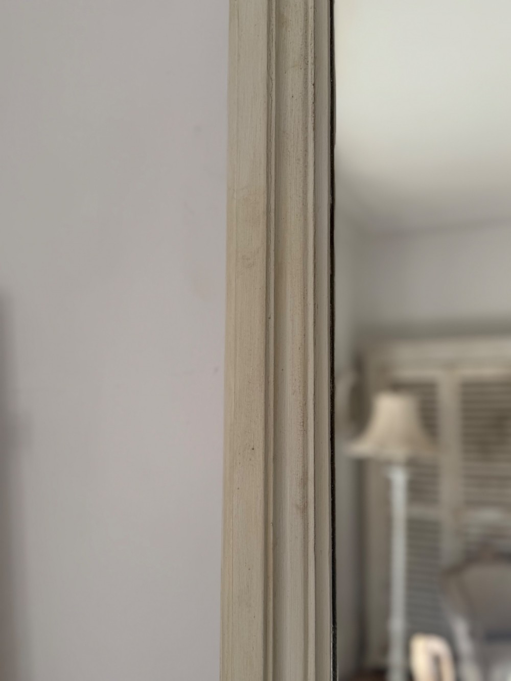 A tall arched mirror featuring a cream painted wooden frame resting on a surface. View VII