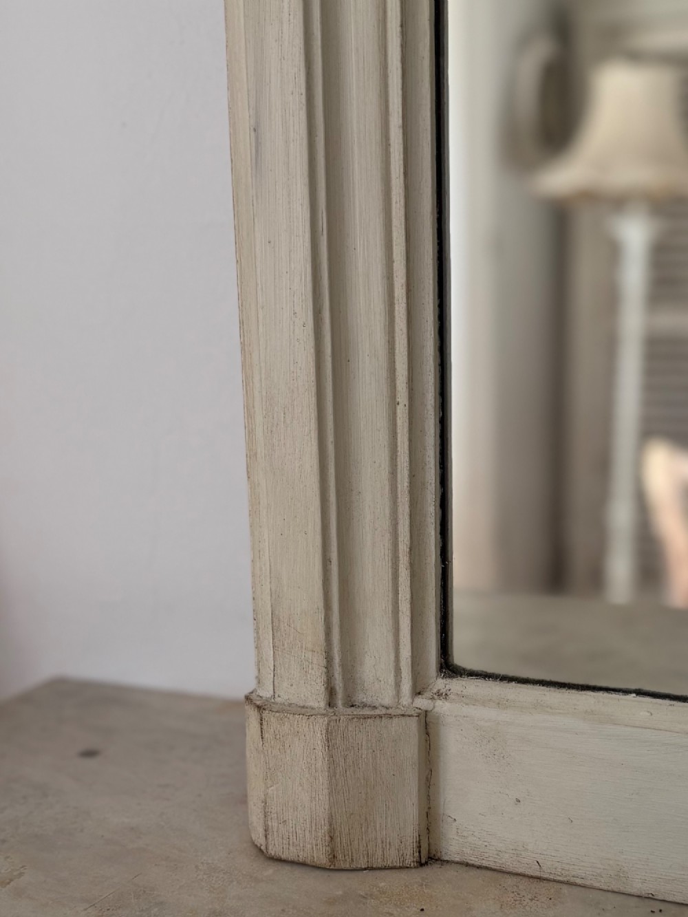 A tall arched mirror featuring a cream painted wooden frame resting on a surface. View VIII