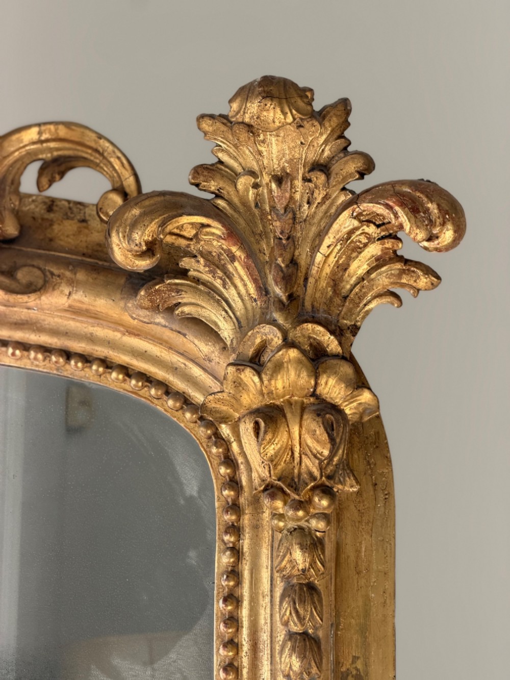 A large 18th century French giltwood mirror featuring an ornate floral shell crest and visible foxing on the mercury glass plate. View III