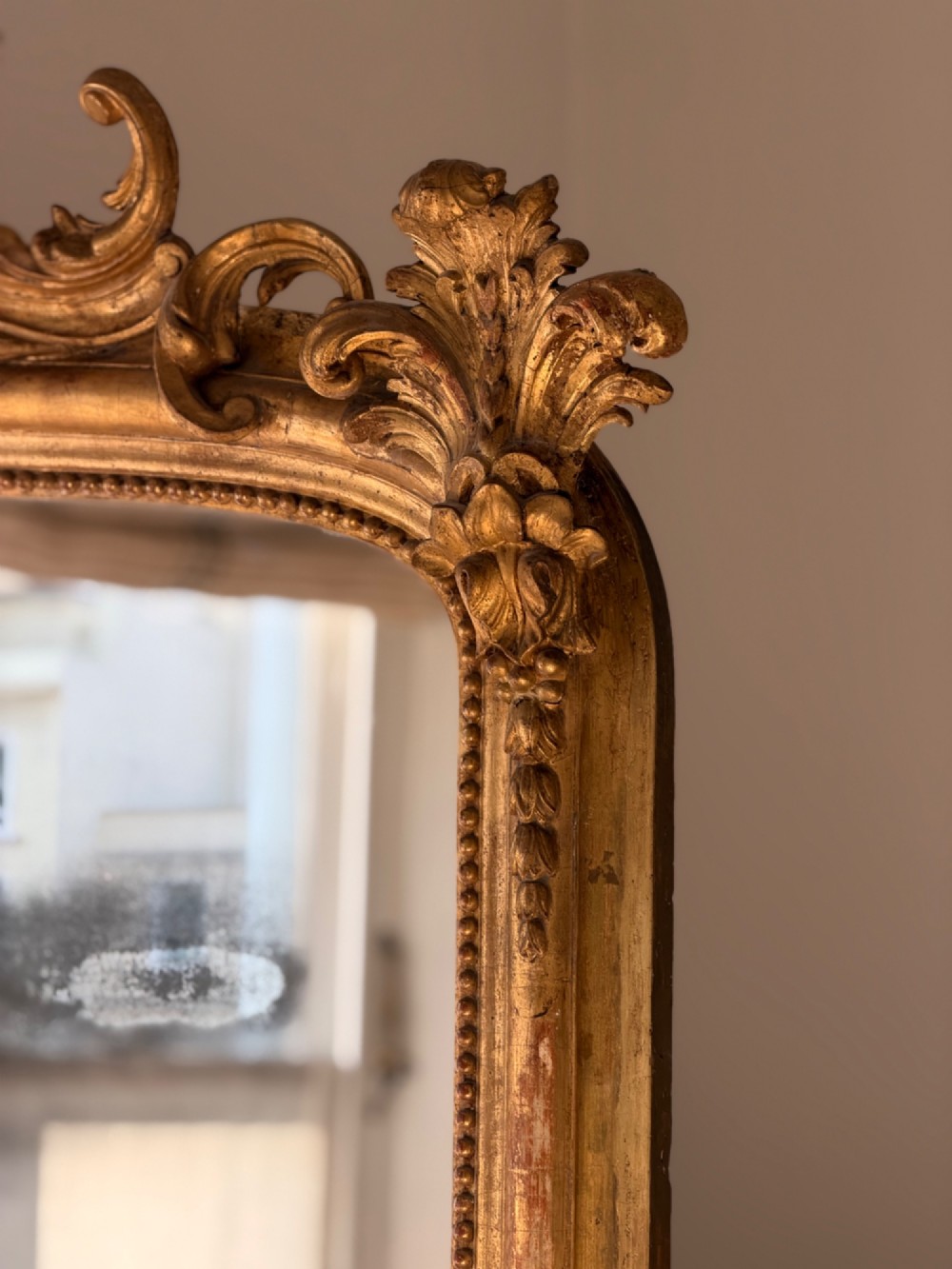 A large 18th century French giltwood mirror featuring an ornate floral shell crest and visible foxing on the mercury glass plate. View VII