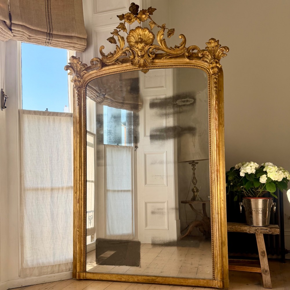 A large 18th century French giltwood mirror featuring an ornate floral shell crest and visible foxing on the mercury glass plate. View VIII