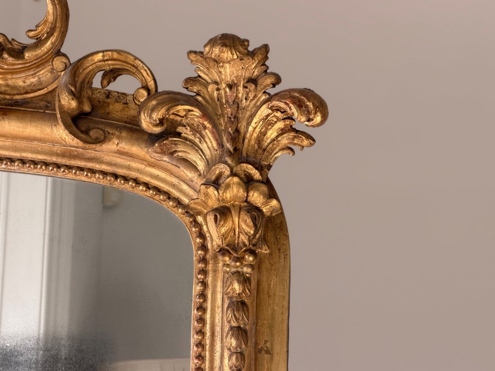 A large 18th century French giltwood mirror featuring an ornate floral shell crest and visible foxing on the mercury glass plate. View X