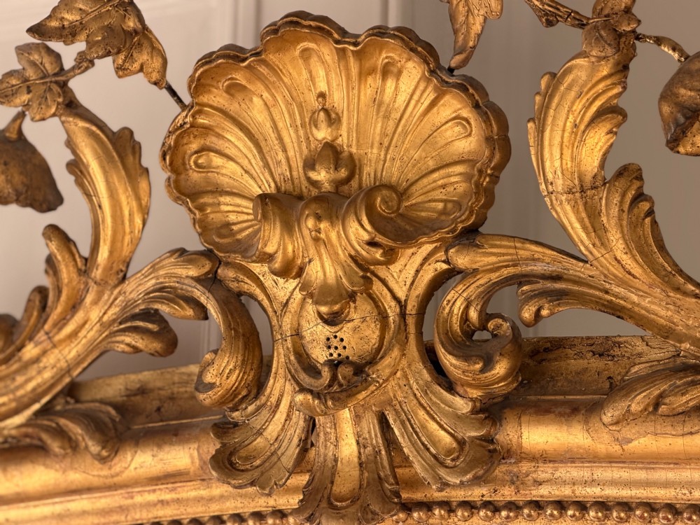 A large 18th century French giltwood mirror featuring an ornate floral shell crest and visible foxing on the mercury glass plate. View XI
