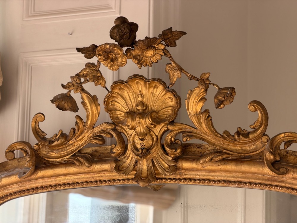 A large 18th century French giltwood mirror featuring an ornate floral shell crest and visible foxing on the mercury glass plate. View XII