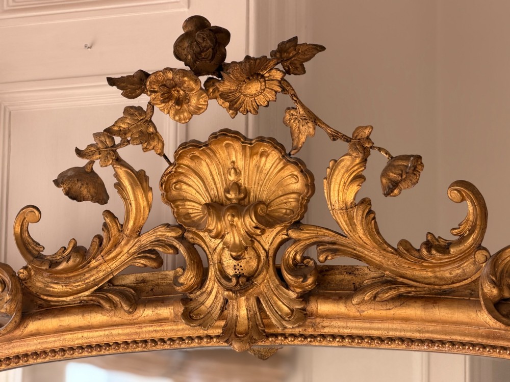 A large 18th century French giltwood mirror featuring an ornate floral shell crest and visible foxing on the mercury glass plate. View XIII