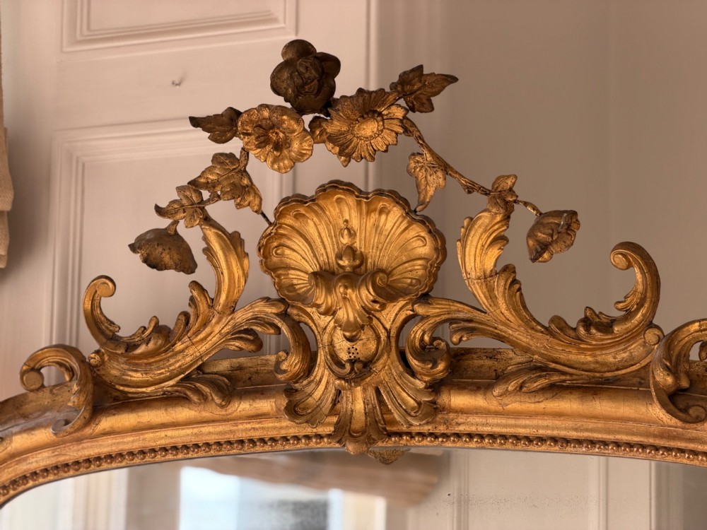 A large 18th century French giltwood mirror featuring an ornate floral shell crest and visible foxing on the mercury glass plate. View XIV