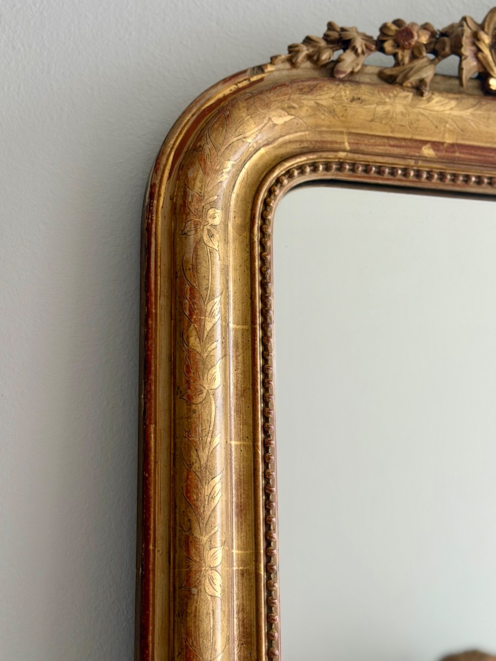 An antique French Louis Philippe giltwood mirror featuring a carved crest and incised floral frame detailing. View III