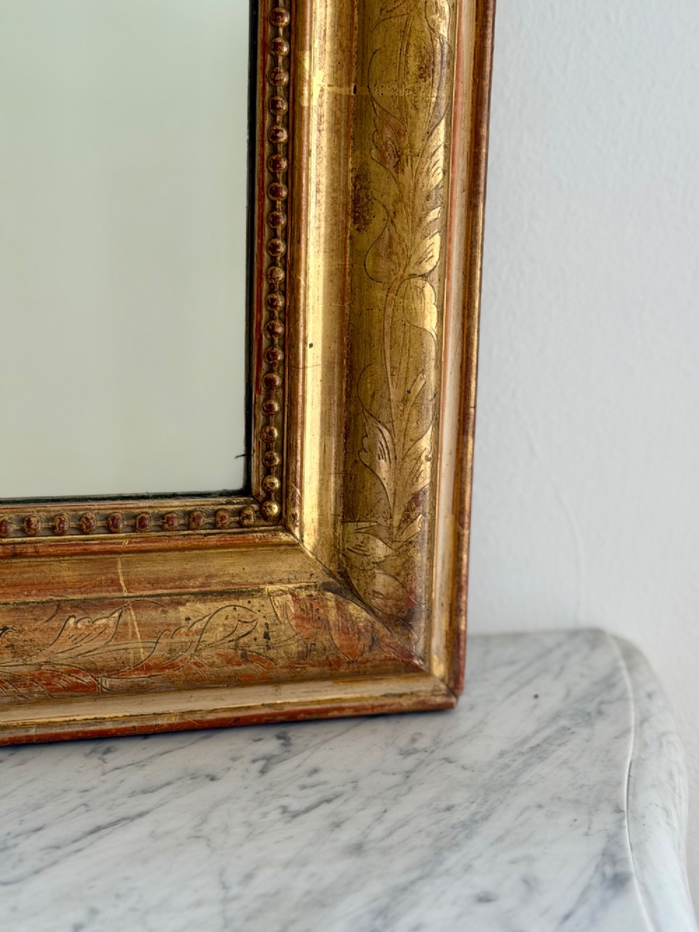 An antique French Louis Philippe giltwood mirror featuring a carved crest and incised floral frame detailing. View VI